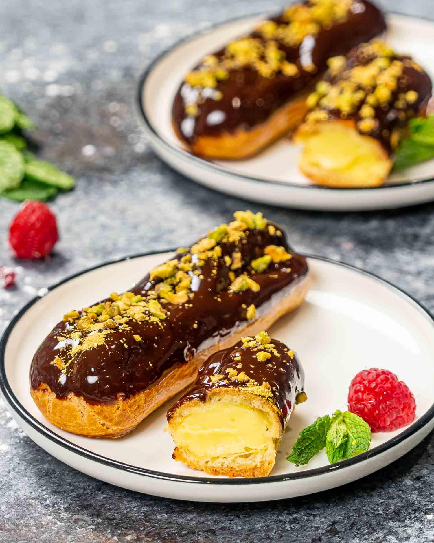 an eclair filled with pastry cream and dipped in chocolate and topped with pistachios.