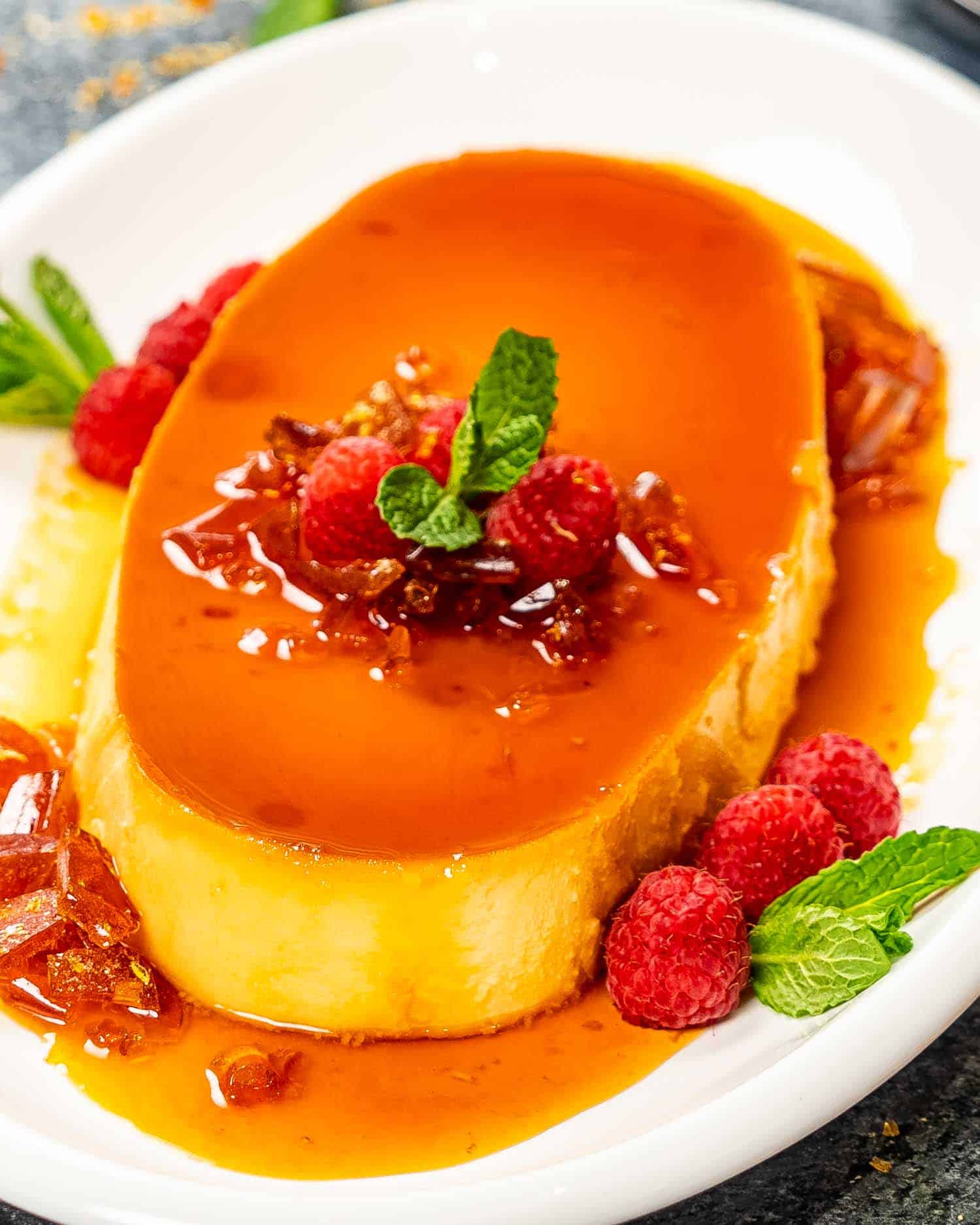 a gorgeous creamy flan on a white oval plate garnished with raspberries.