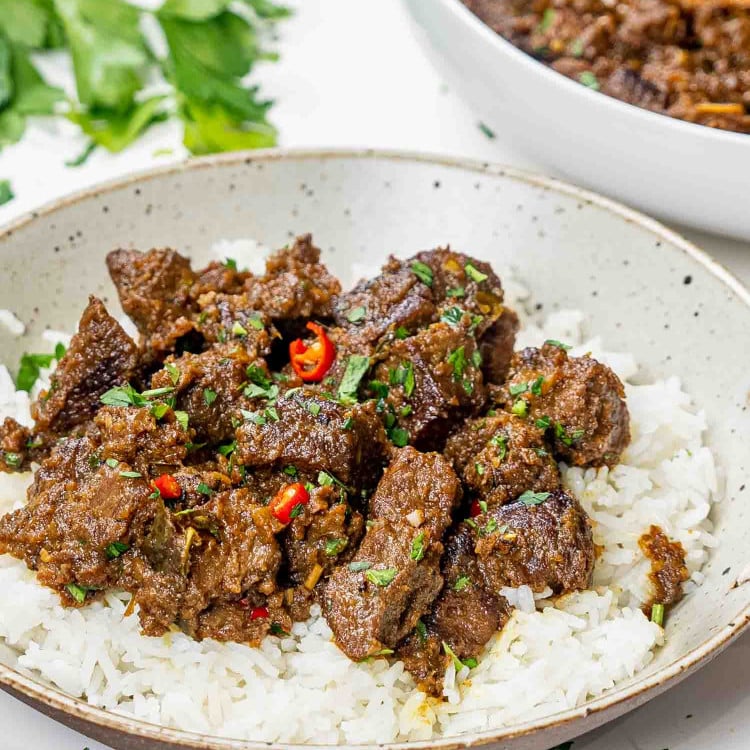 a serving of beef rendang on a bed of rice garnished with red chilies.