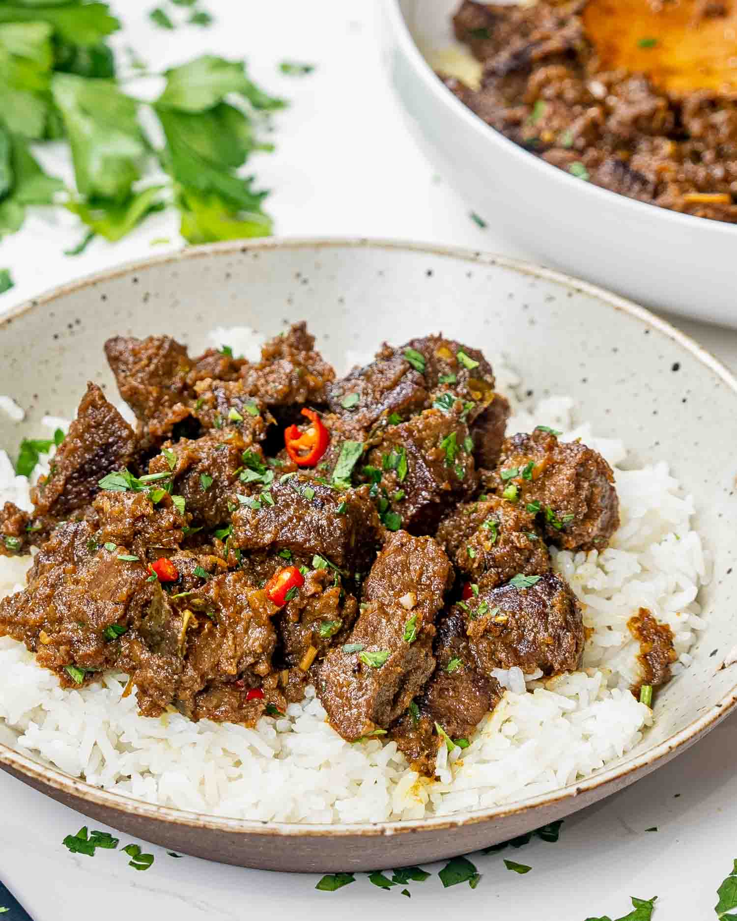 a serving of beef rendang on a bed of rice garnished with red chilies.