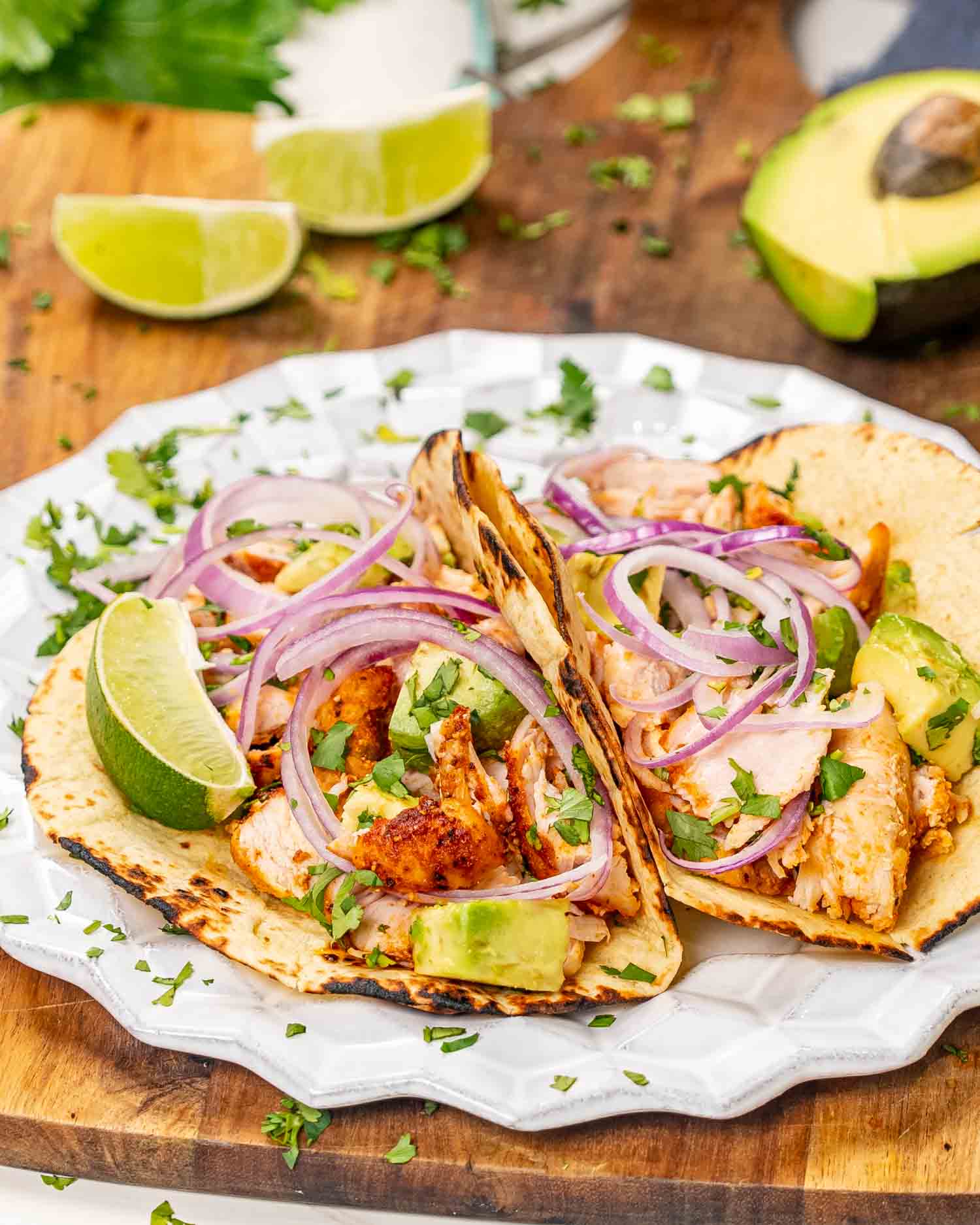 two chicken tacos with avocados and red onion on a white plate.
