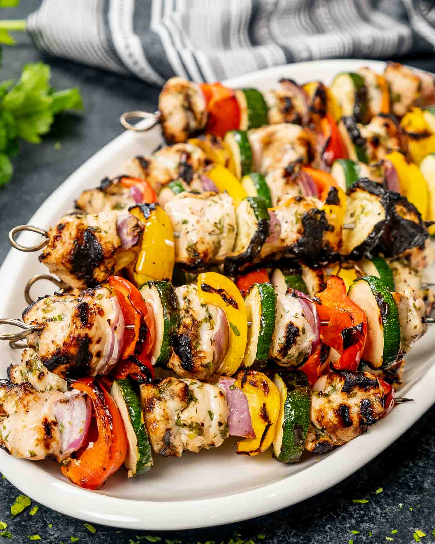 a few skewers of grilled chicken kebabs on a white platter.