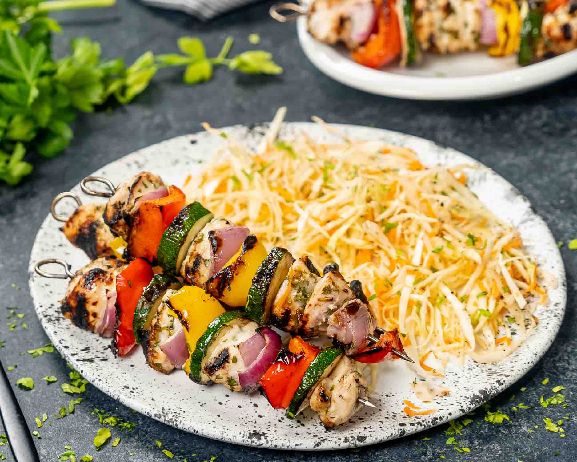 2 grilled chicken kebabs skewers on a plate with cabbage salad.