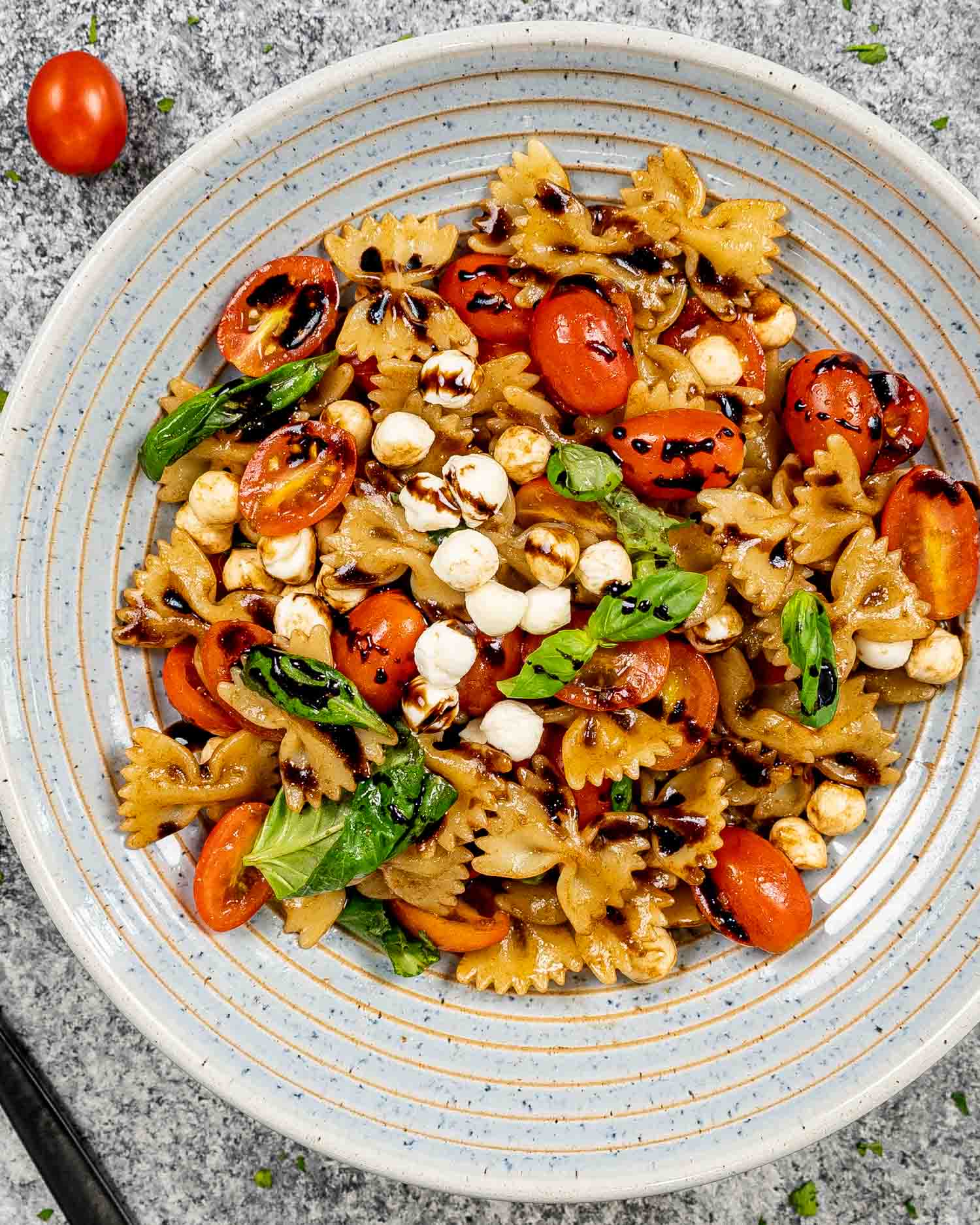 a blue bowl loaded with caprese pasta salad drizzled with extra balsamic glaze and garnished with fresh basil.