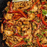 freshly made chili garlic chicken in a skillet garnished with cilantro and lime wedges.