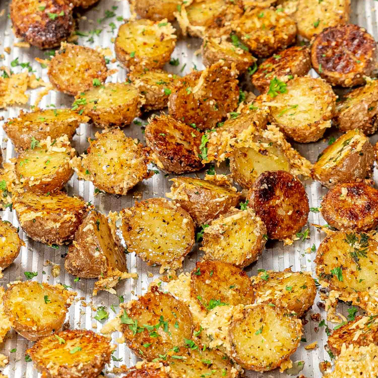 freshly baked crispy parmesan potatoes on a baking sheet garnished with parmesan cheese and parsley.