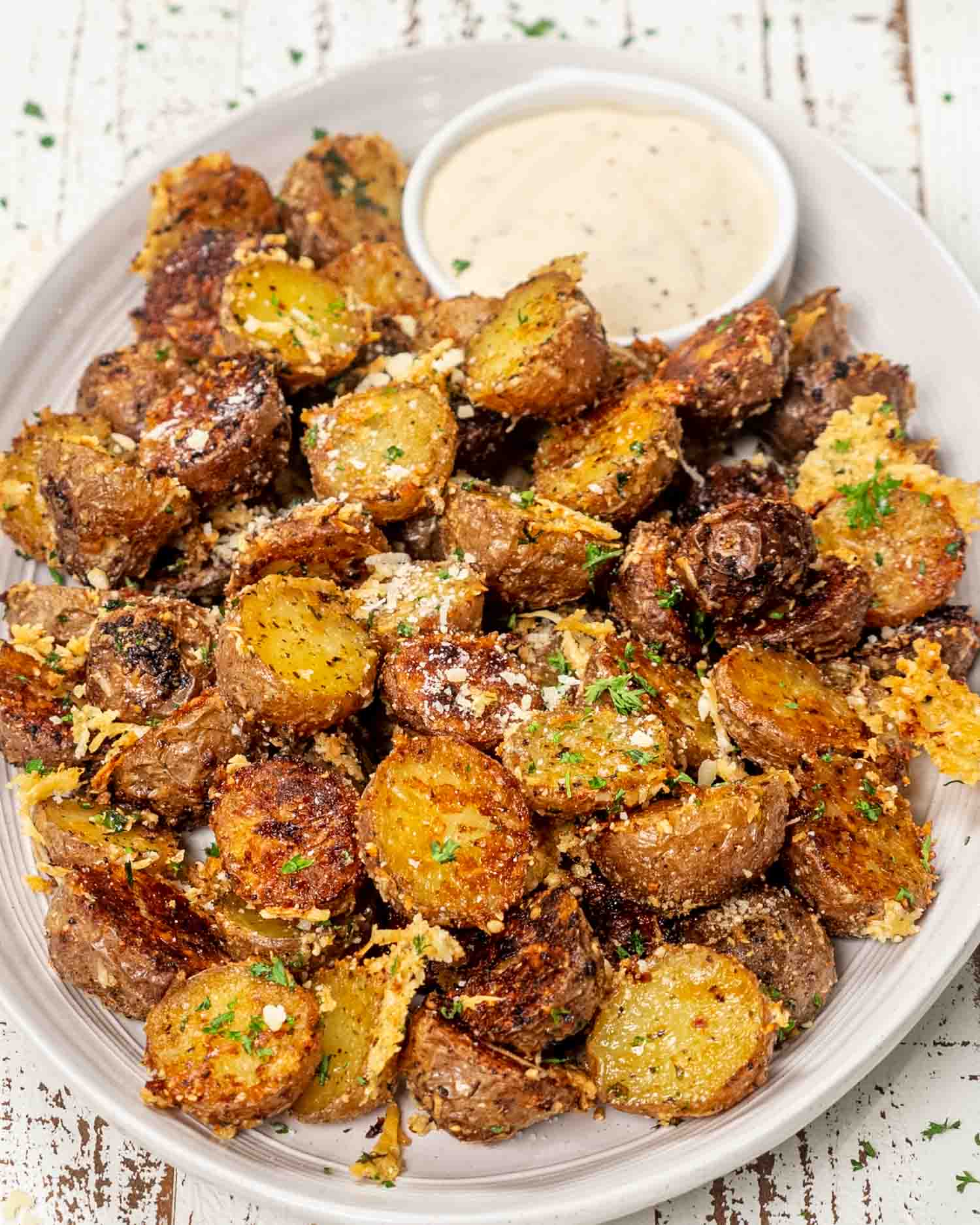 crispy parmesan potatoes on a white platter garnished with parmesan cheese and parsley.
