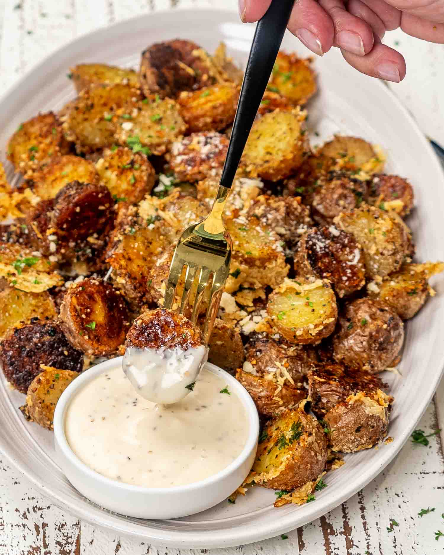 crispy parmesan potatoes on a white platter garnished with parmesan cheese and parsley.