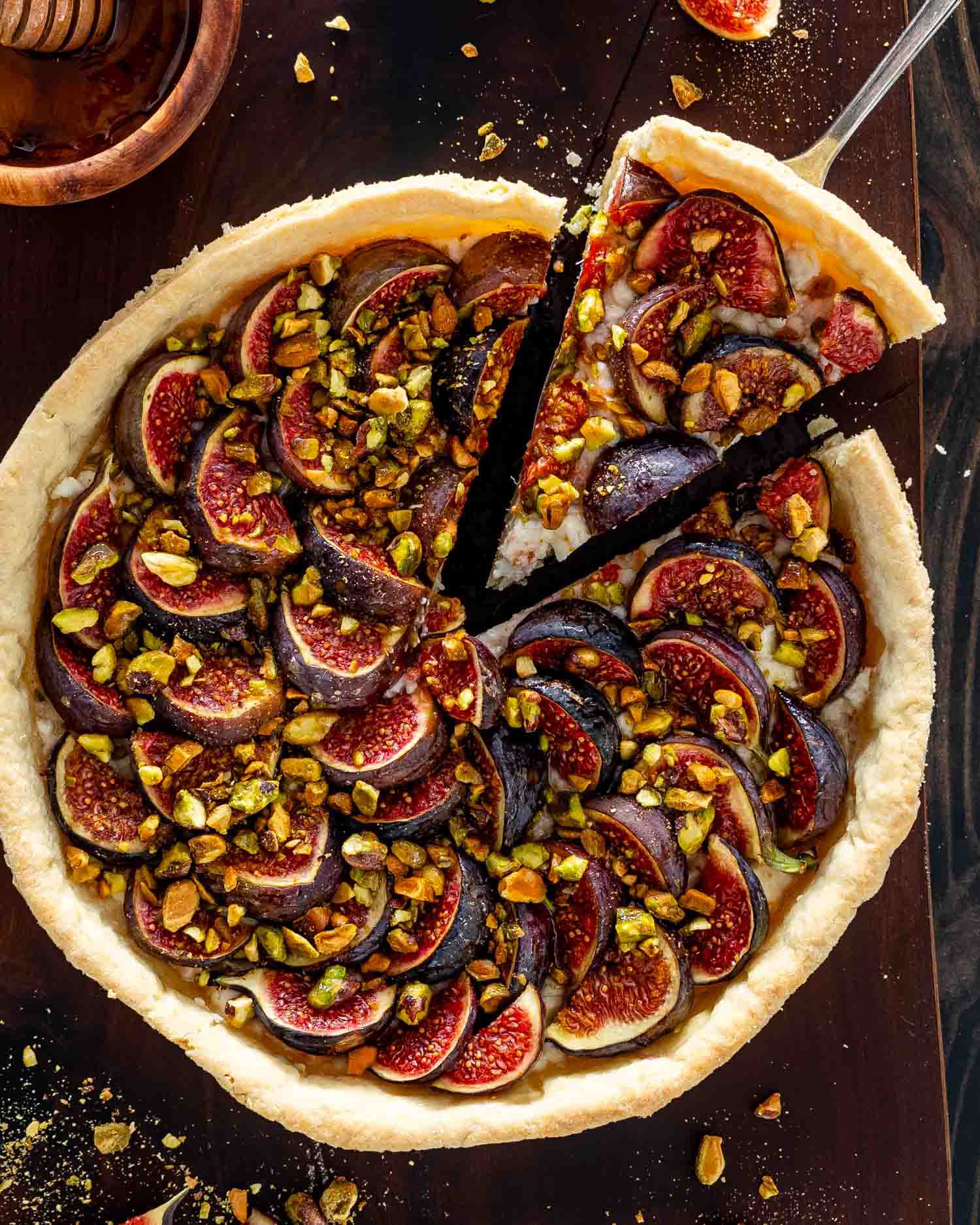 a fig tart on a cutting board with goat cheese and pistachios on a cutting board.