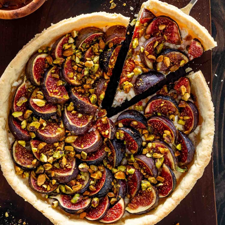 a fig tart on a cutting board with goat cheese and pistachios on a cutting board.