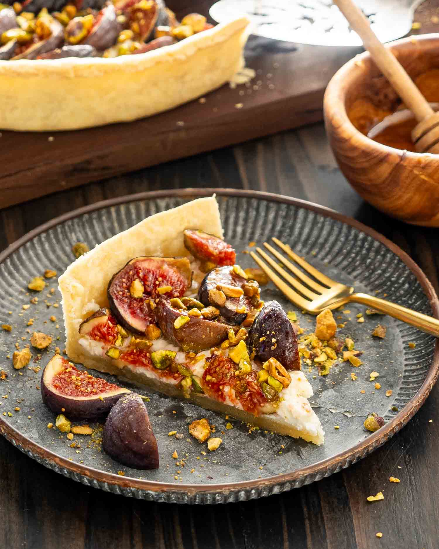 a slice of fig tart with goat cheese and pistachios on a metal plate.