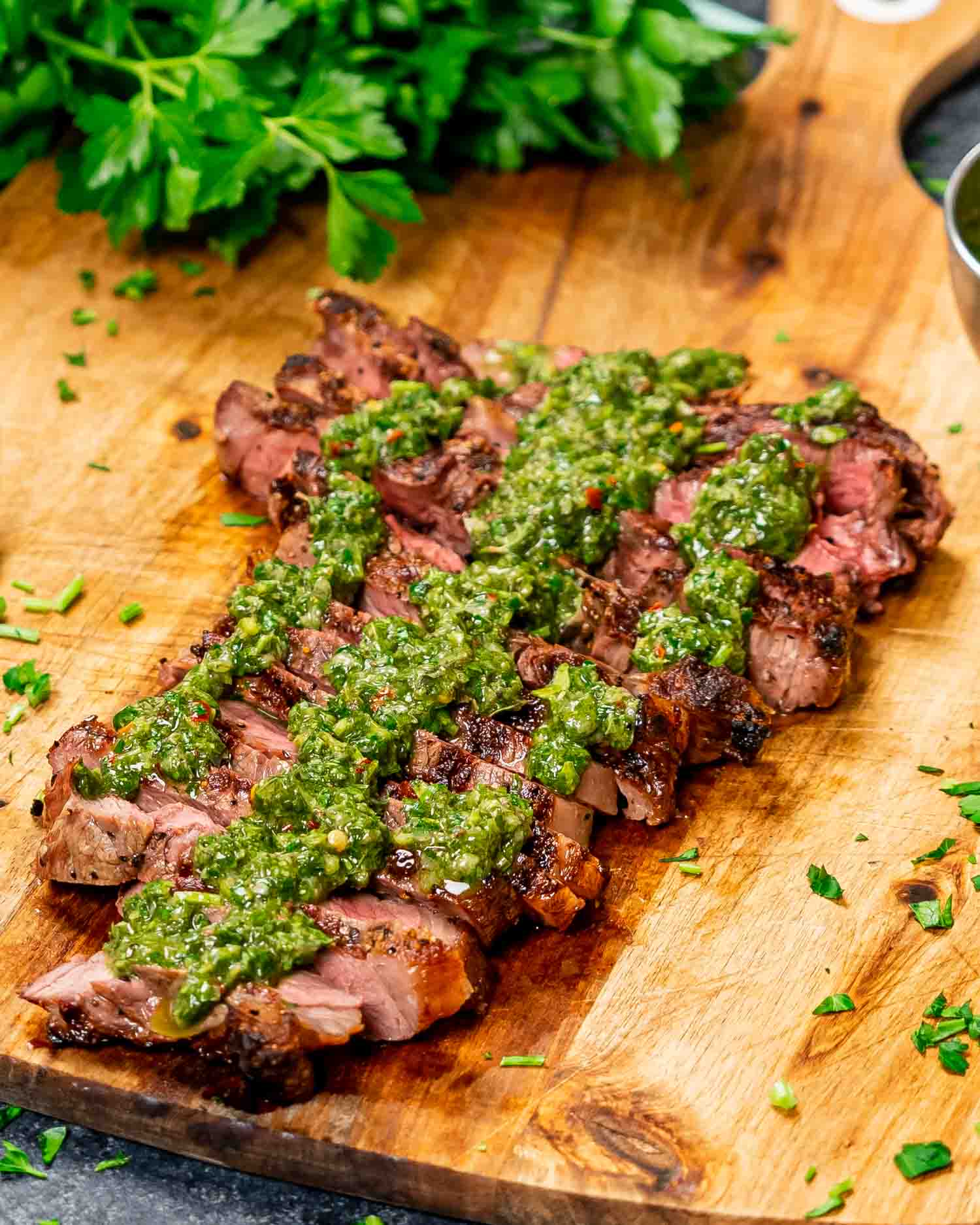 a sliced up grilled ribeye drizzled with chimichurri sauce on a cutting board.