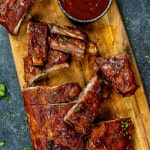 cut up oven baked bbq ribs with bbq sauce on a cutting board.