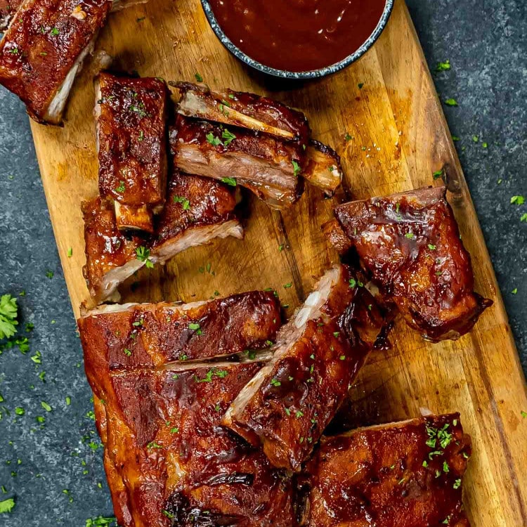 cut up oven baked bbq ribs with bbq sauce on a cutting board.