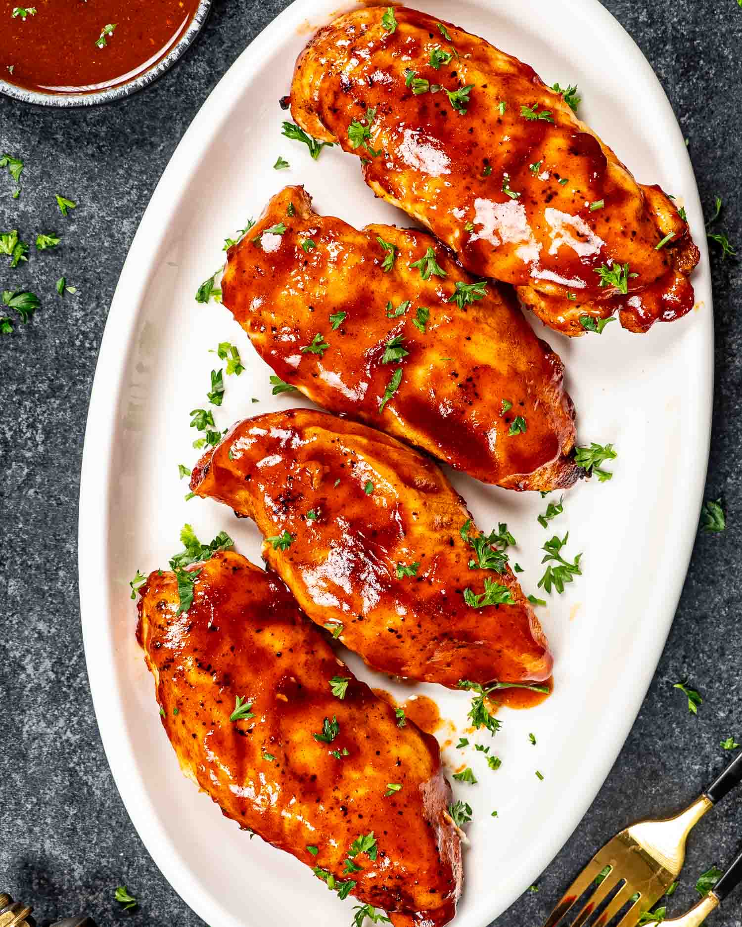 bbq chicken breasts on a white platter garnished with parsley.
