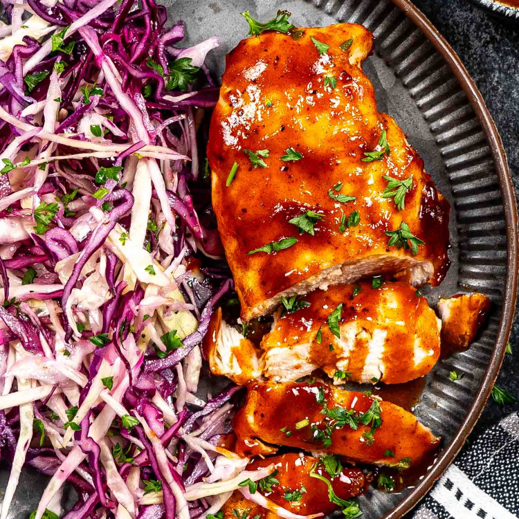bbq chicken breast with coleslaw on a plate garnished with parsley.