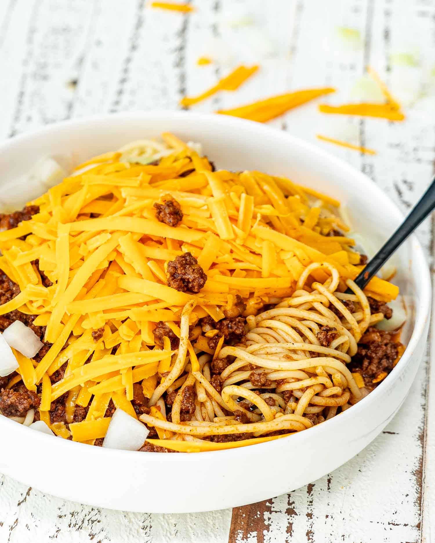 a white bowl loaded with spaghetti and cincinnati chili, onions and cheddar cheese.