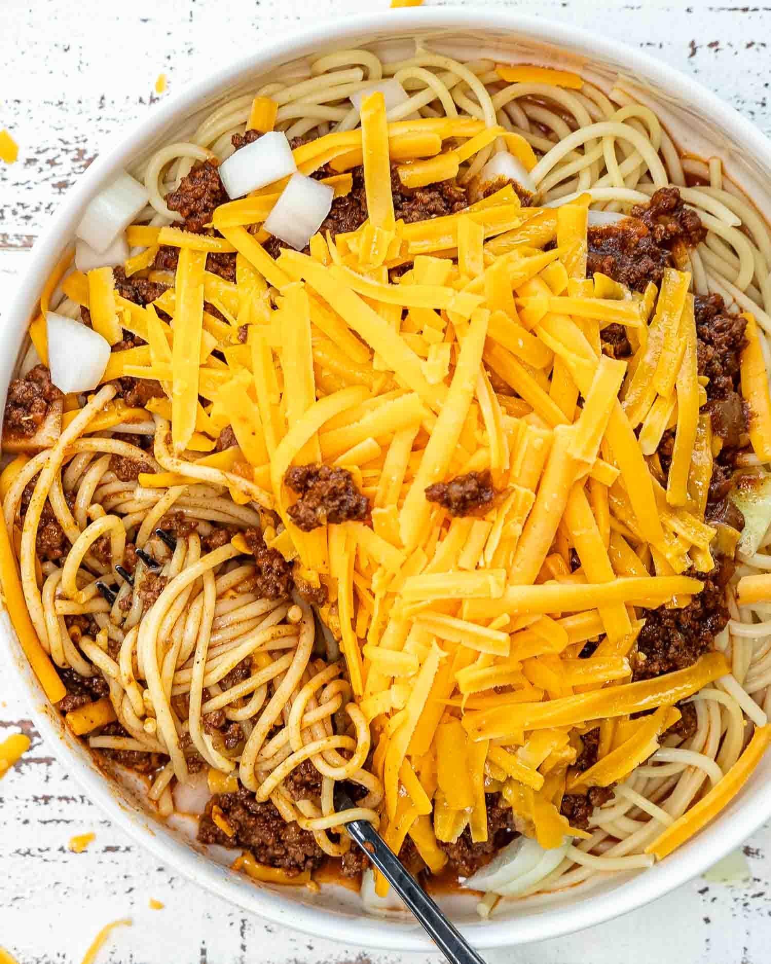 a white bowl loaded with spaghetti and cincinnati chili, onions and cheddar cheese.