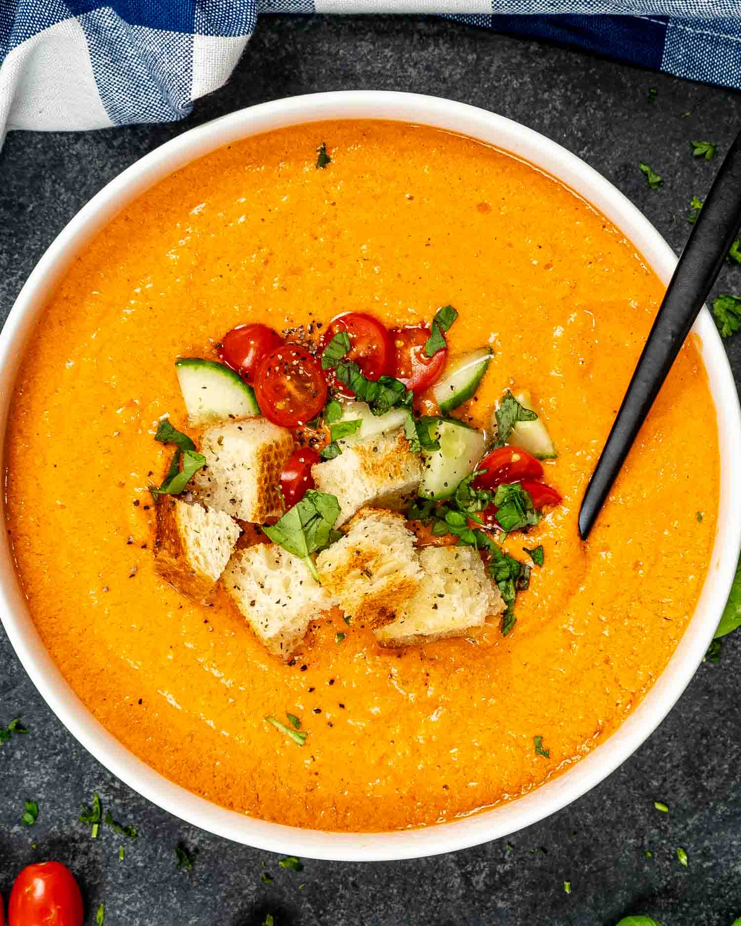 a white bowl loaded with fresh gazpacho and topped with croutons, chopped tomatoes and cucumber and a sprinkle of basil.