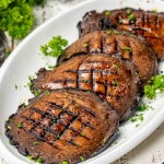 4 grilled portobello mushrooms on a white platter garnished with parsley.