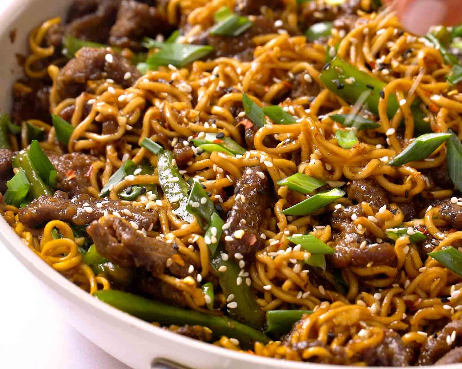 Overhead view of Mongolian Beef Ramen in a skillet with glossy sauce, green bell peppers, and sesame seeds.