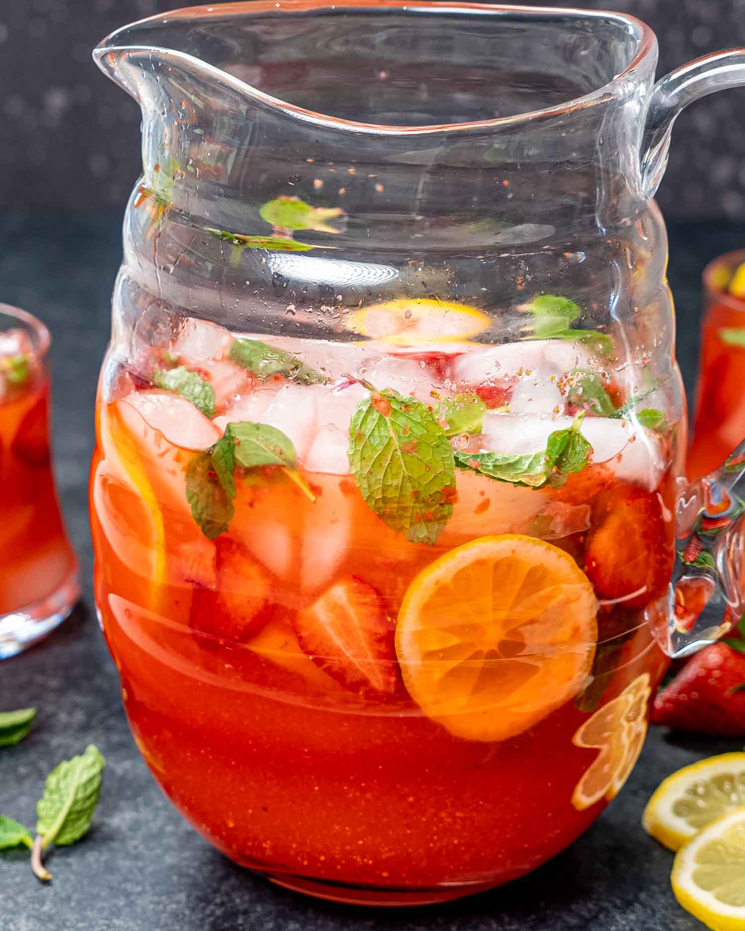 a pitcher full of strawberry lemonade garnished with mint, lemon slices and strawberries.