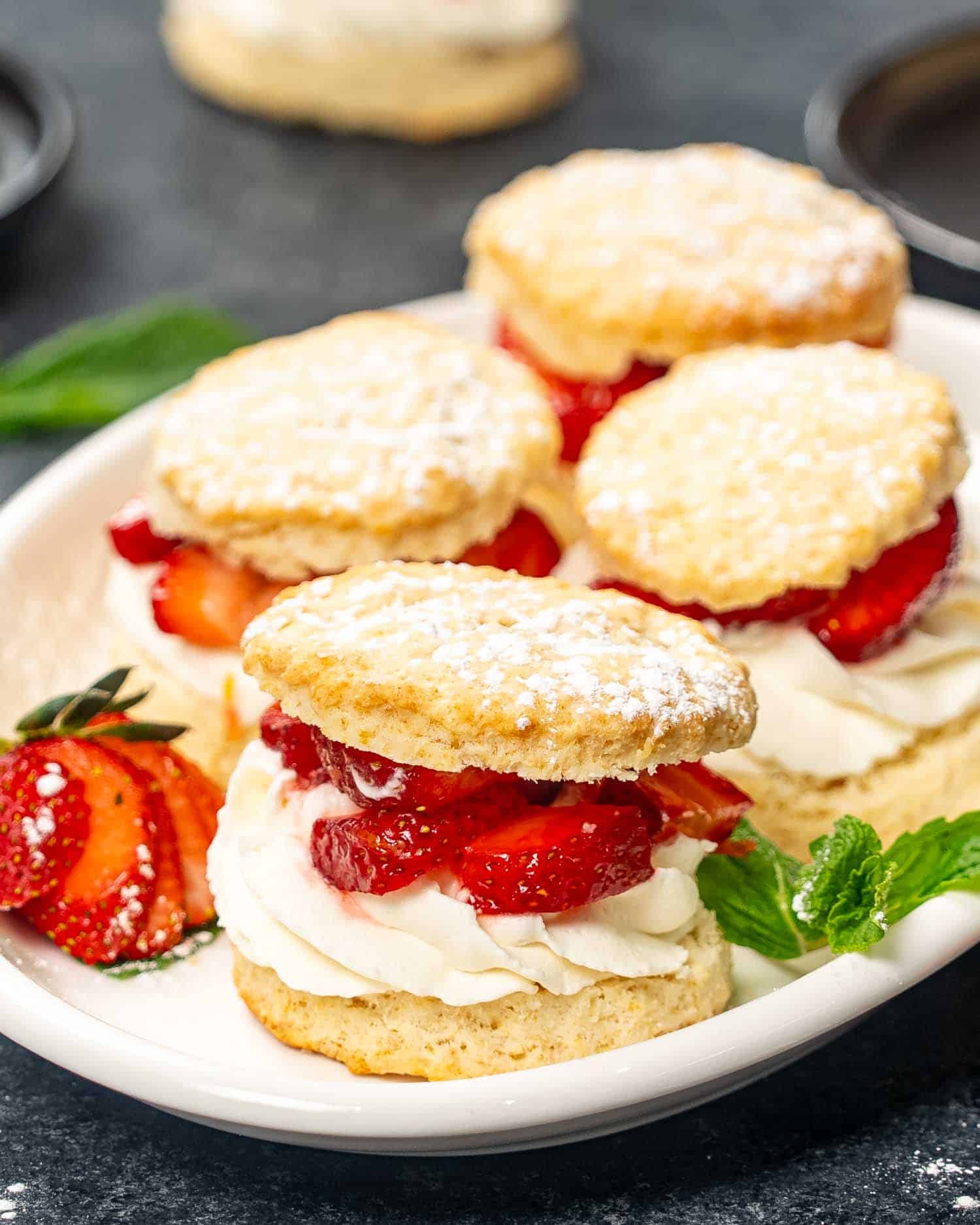 a few strawberry shortcakes on a white platter sprinkled with powdered sugar.