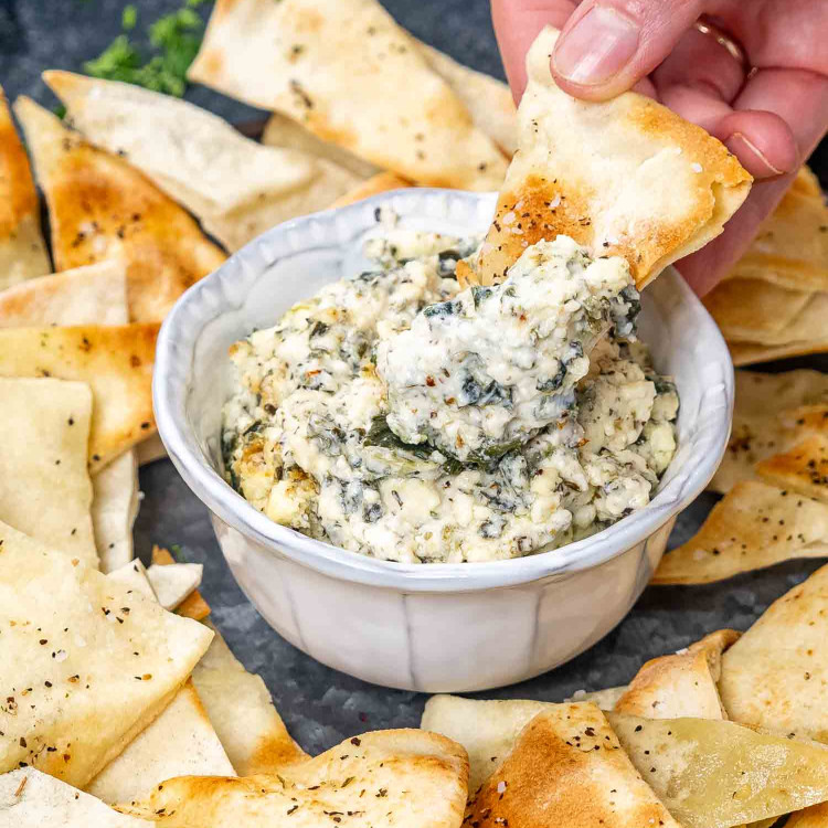 a small bowl with baked feta spinach dip with pita bread for dipping.