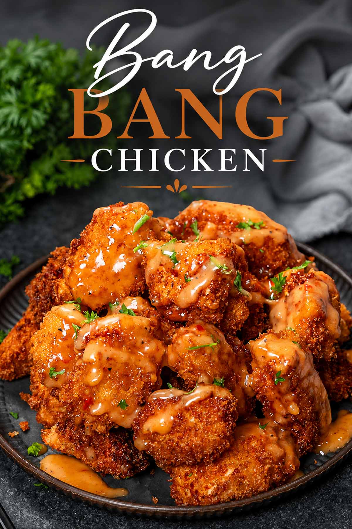 Crispy Bang Bang Chicken bites drizzled with creamy sweet and spicy sauce, garnished with parsley on a dark plate.