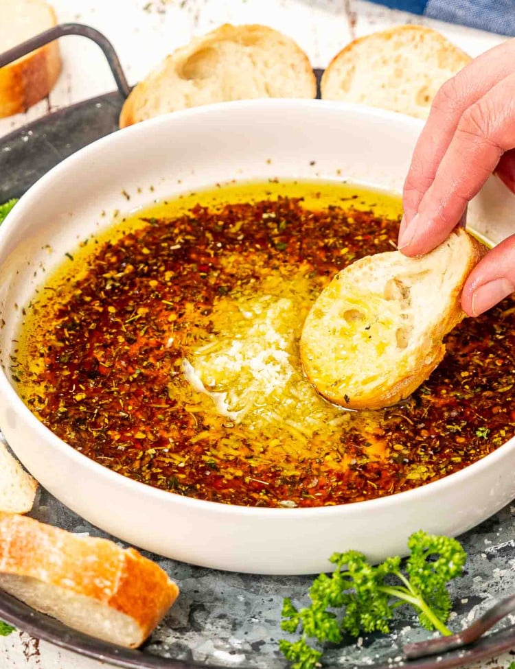 a hand dipping a piece of baguette in a bowl with bread dipping oil.
