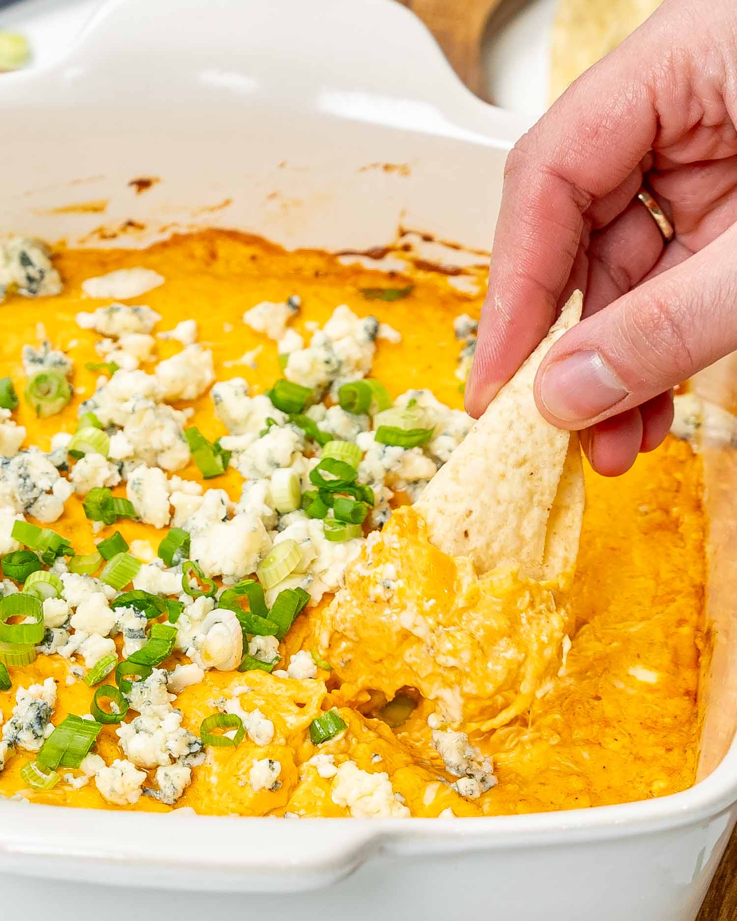 buffalo chicken dip in a square baking dish garnished with blue cheese and green onions.