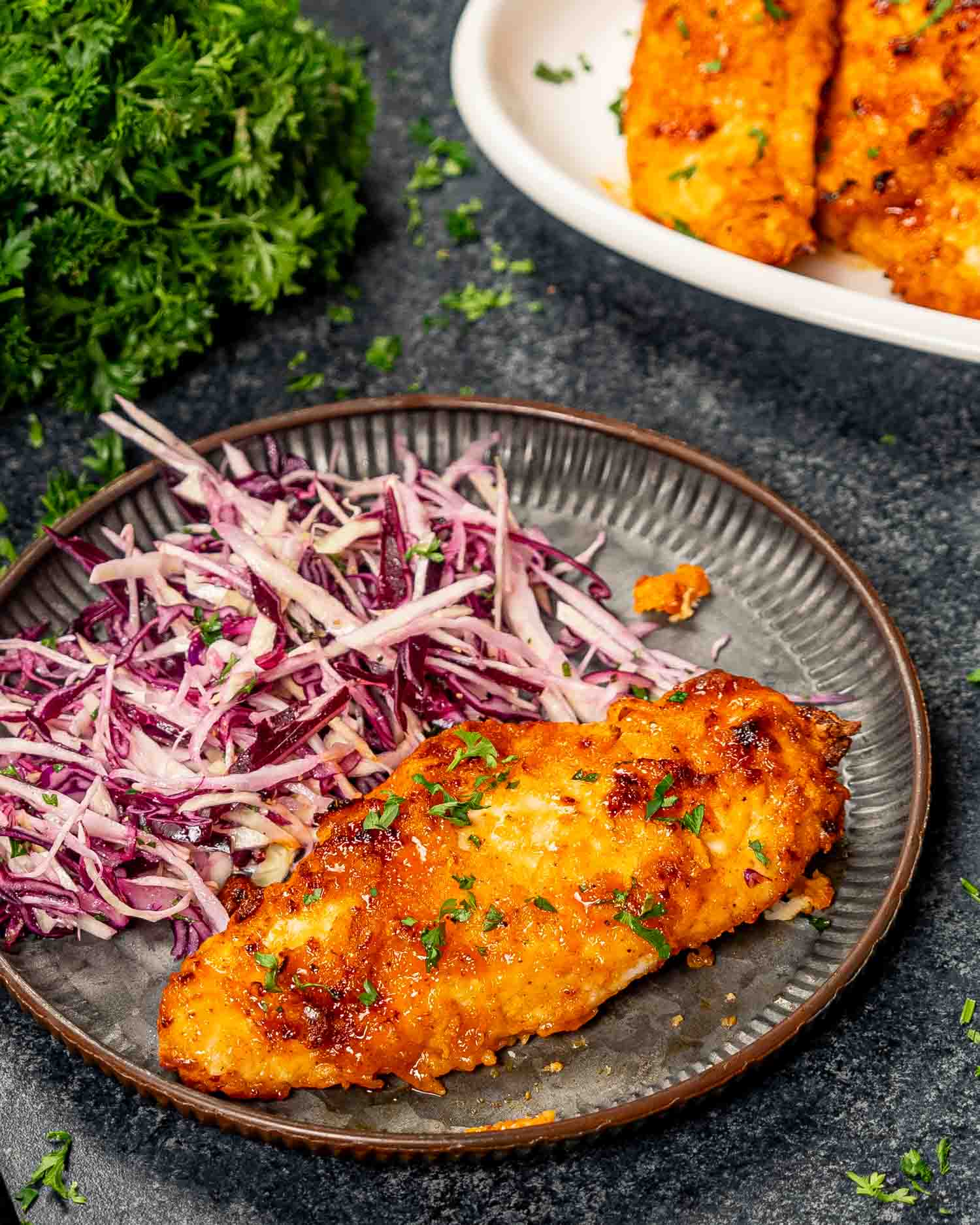 a hot honey chicken breast in a metal plate along a cabbage salad.