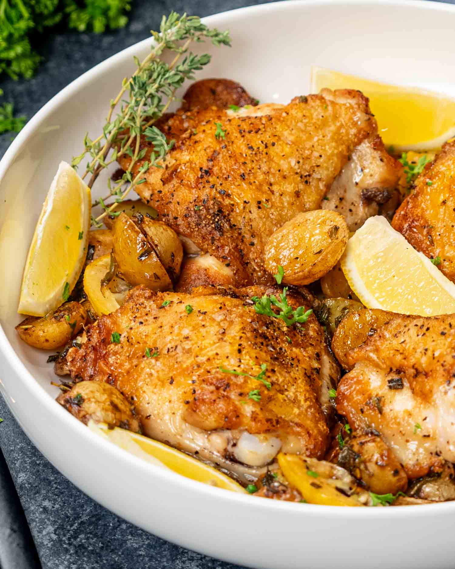 lemon herb chicken and potatoes in a white bowl garnished with lemon wedges and rosemary.