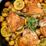 lemon herb chicken and potatoes in a skillet garnished with rosemary and lemon slices.