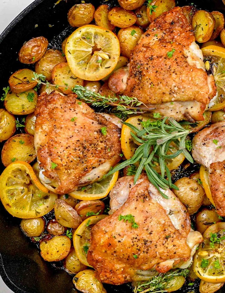 lemon herb chicken and potatoes in a skillet garnished with rosemary and lemon slices.