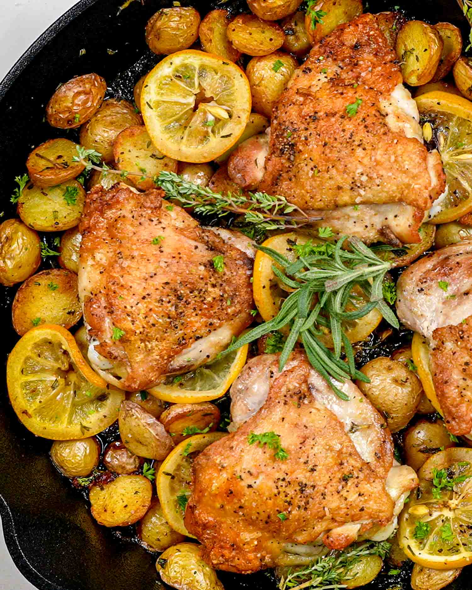 lemon herb chicken and potatoes in a skillet garnished with rosemary and lemon slices.