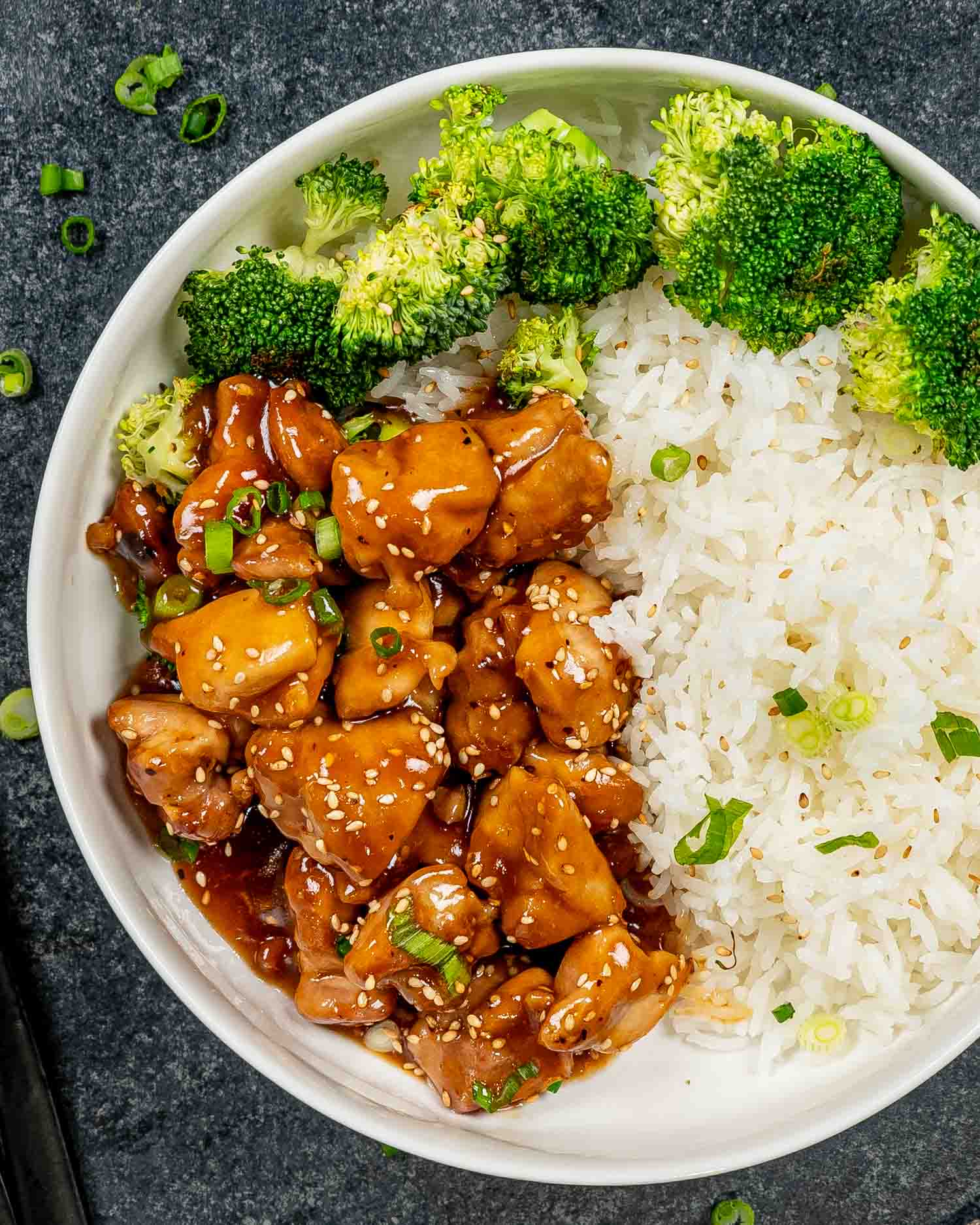 teriyaki chicken in a white bowl with some cooked rice and steamed broccoli.
