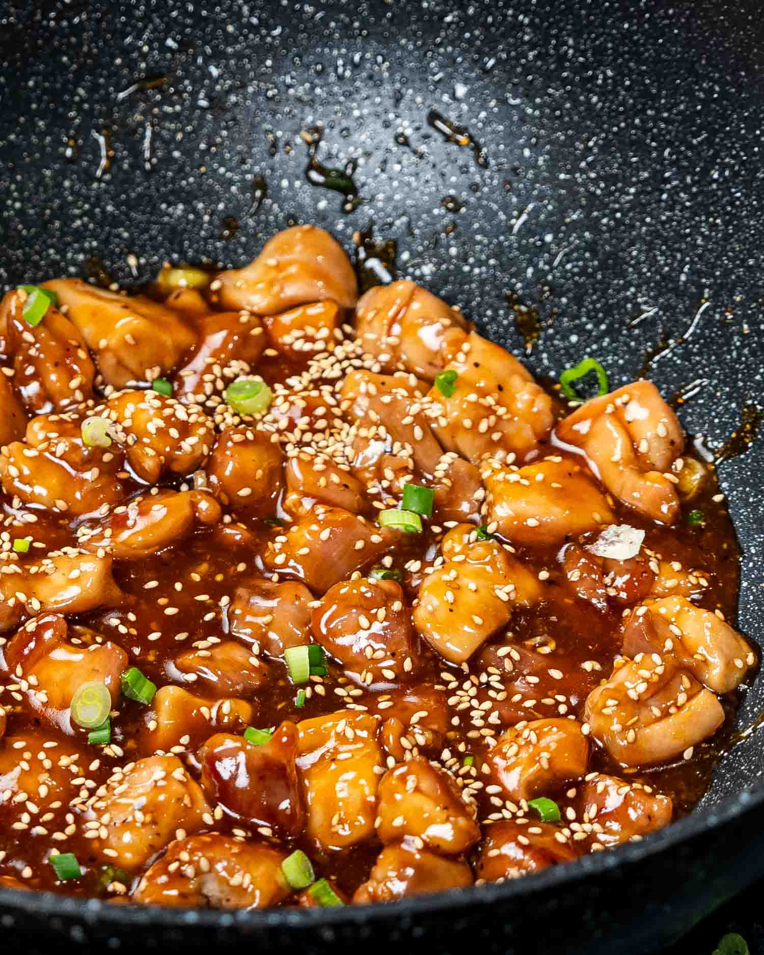 teriyaki chicken garnished with sesame seeds and green onions in a wok.