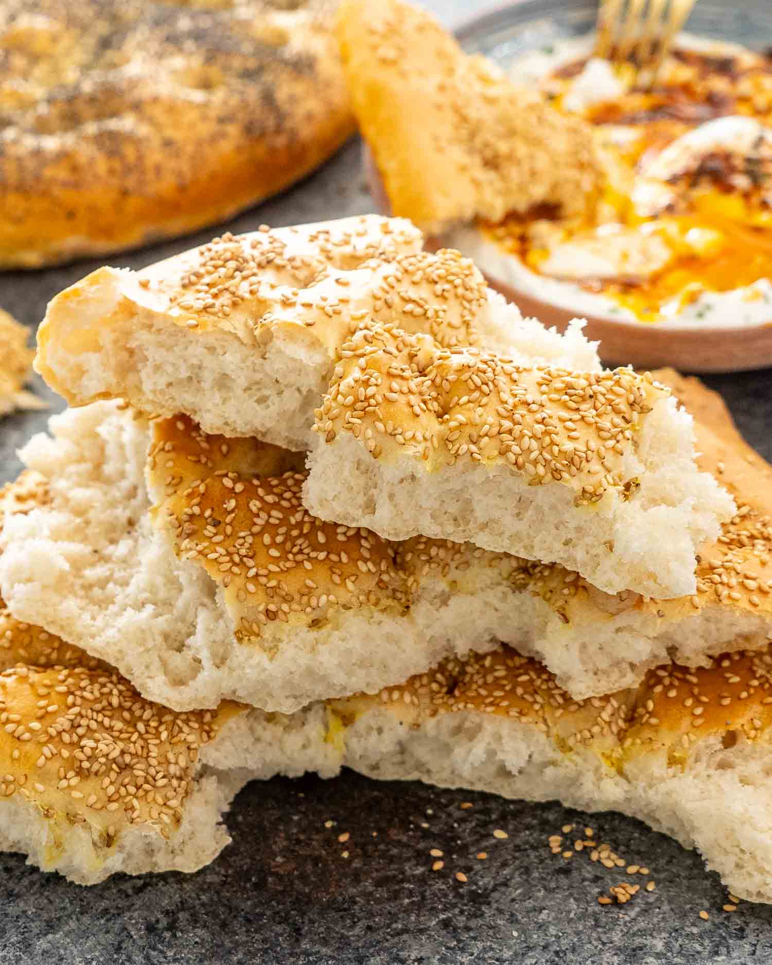 turkish bread, one broken in half on a table, topped with sesame seeds and poppy seeds.