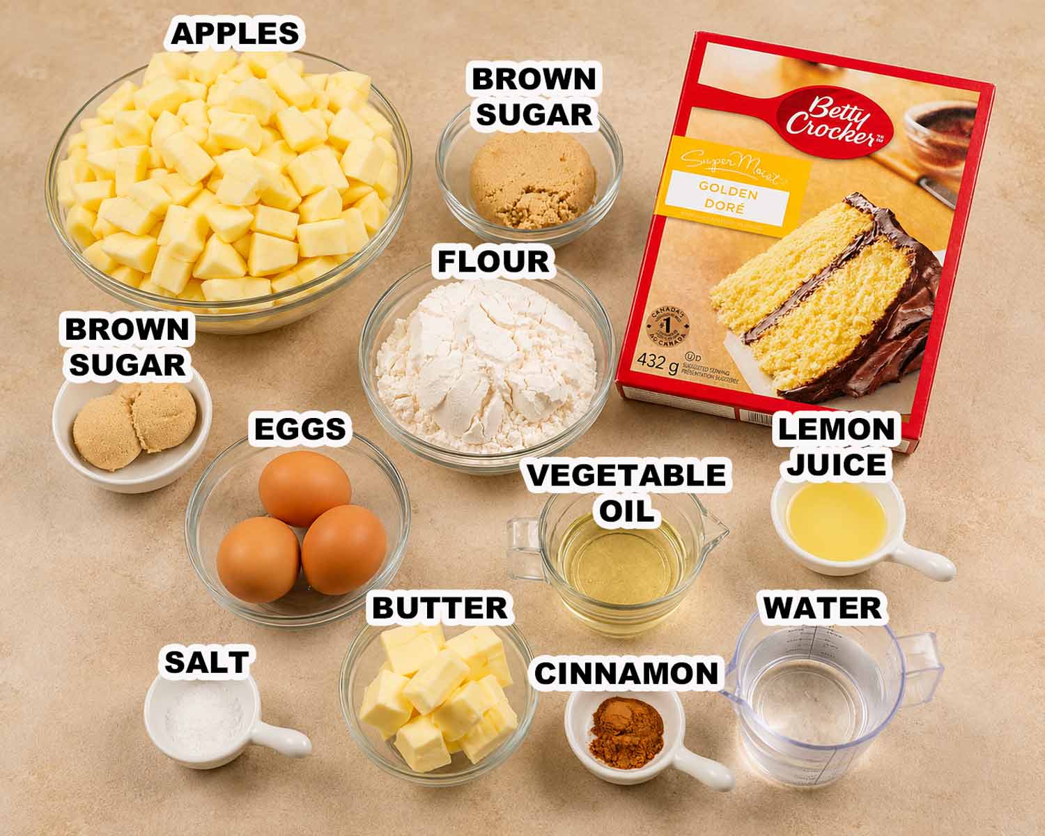 Apple pie cake ingredients including apples, flour, brown sugar, eggs, butter, cinnamon, lemon juice, oil, water, and cake mix.