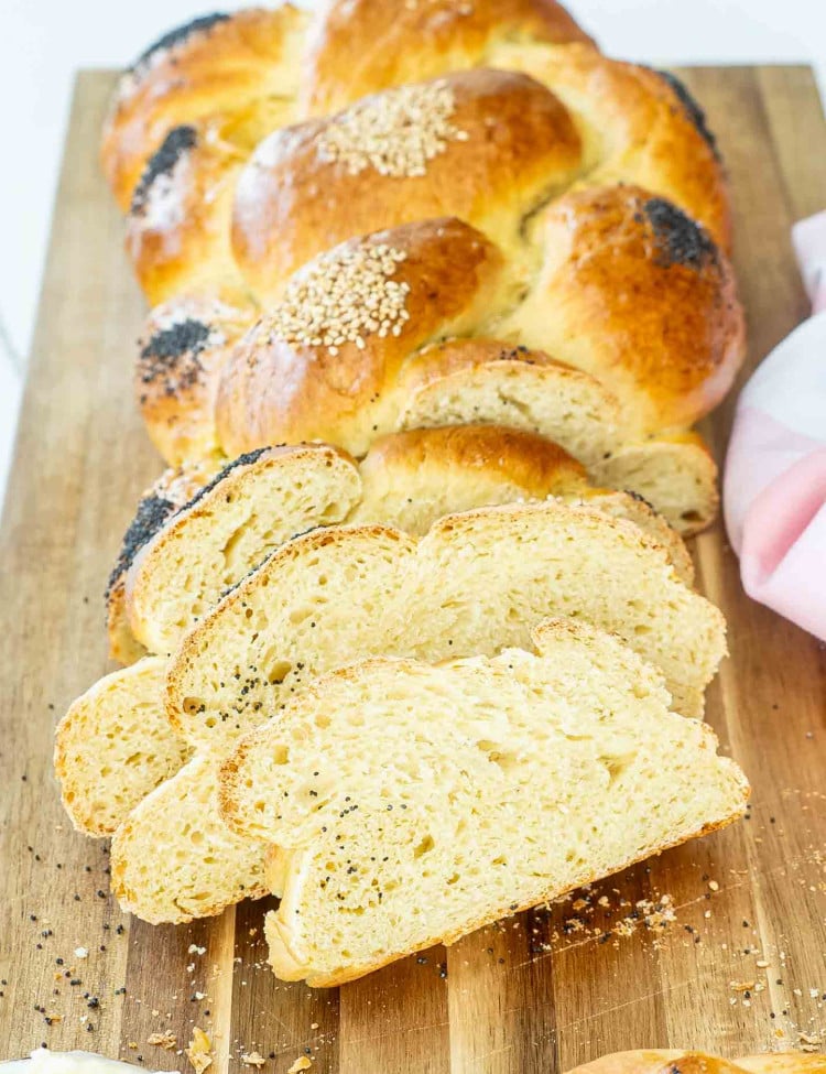 a gorgeous, freshly baked challah bread, half of it sliced on a cutting board.