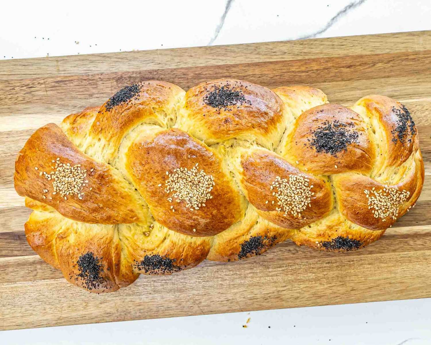 a gorgeous challah bread with sesame and poppy seeds on a cutting board.