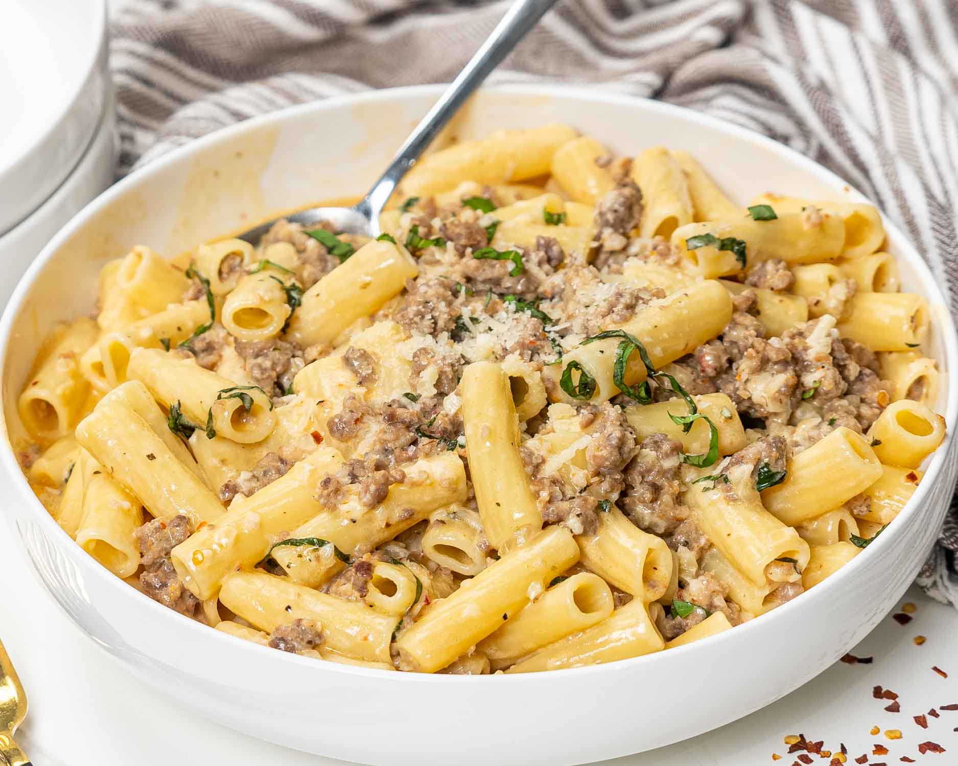 a serving of creamy italian sausage pasta in a white bowl.
