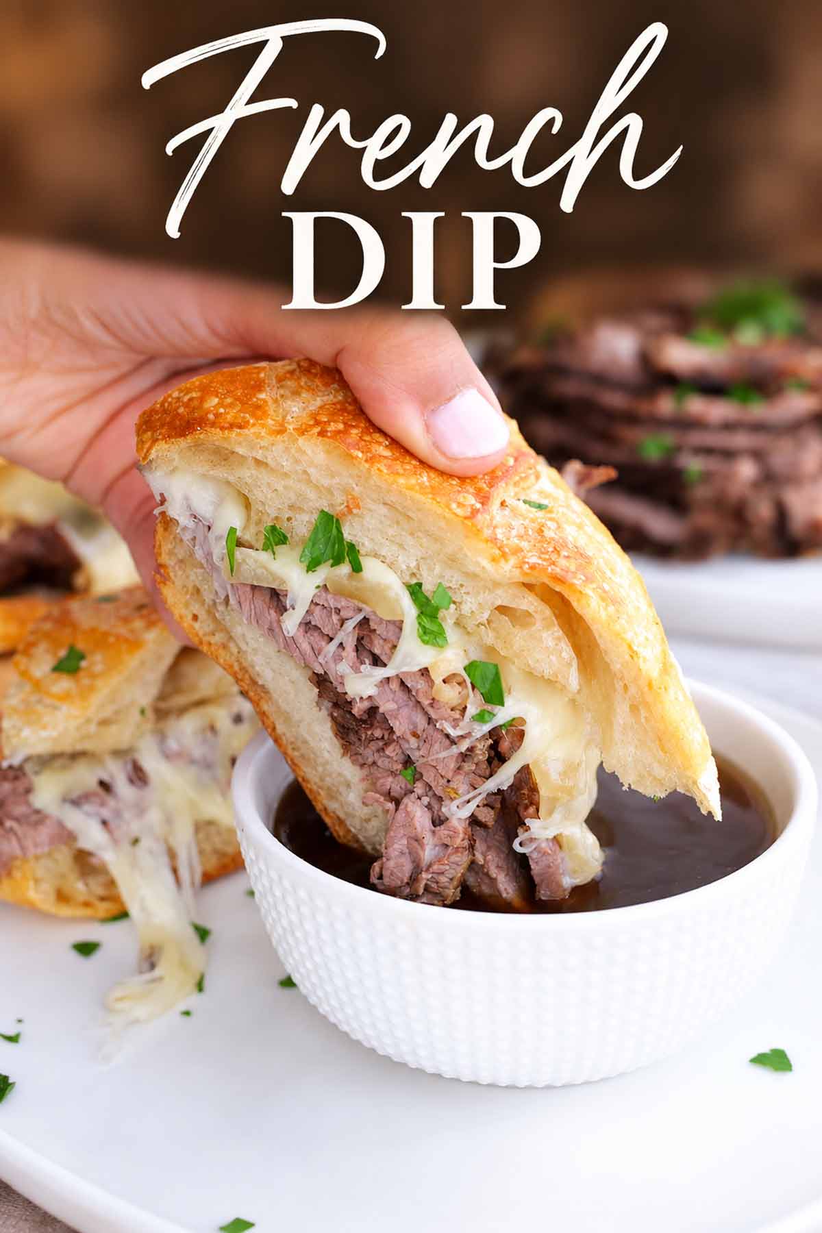French dip sandwich stuffed with tender beef and melted cheese being dipped into warm au jus, with an elegant title overlay.