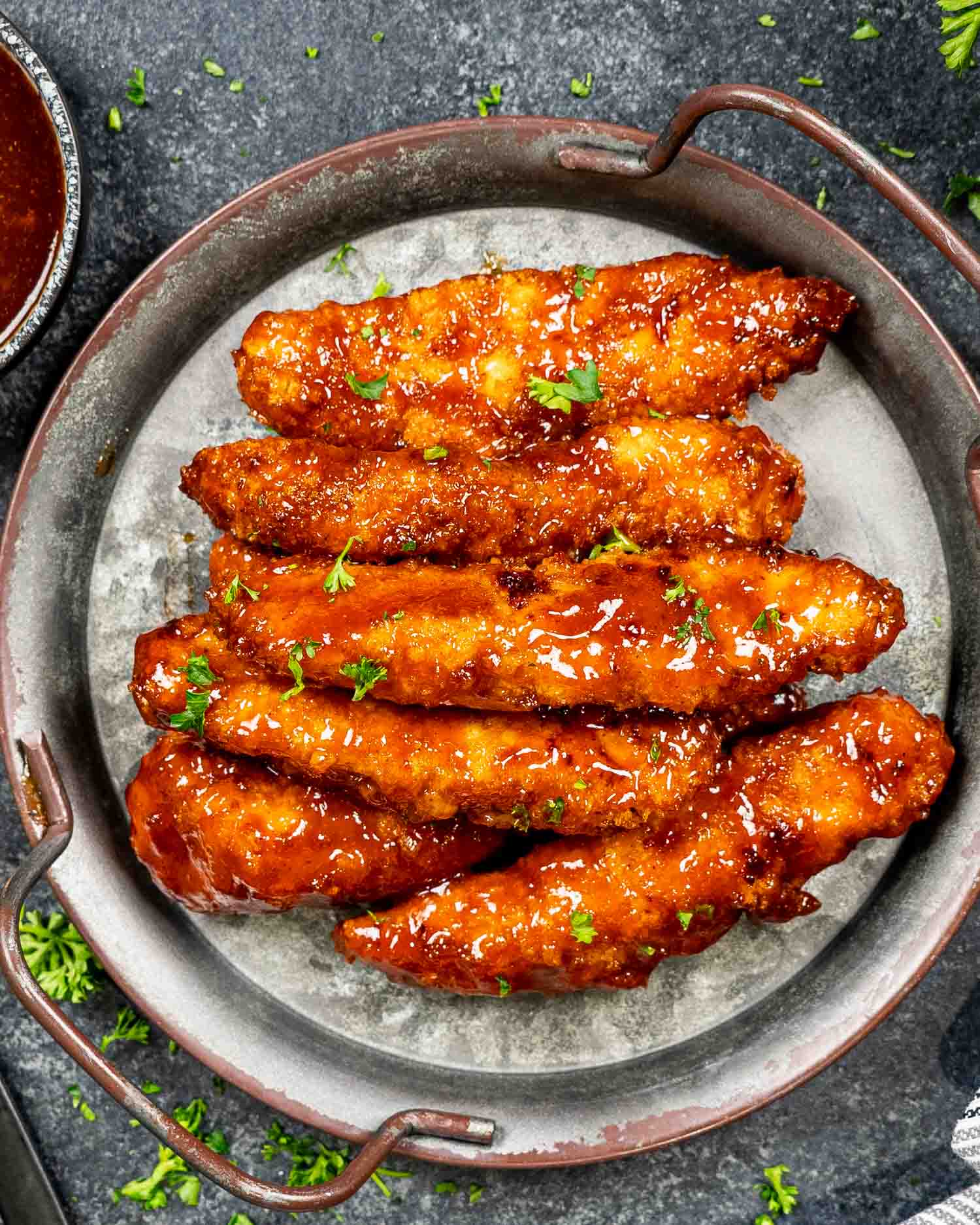 air fried honey bbq chicken tenders on a metal plate garnished with parsley.