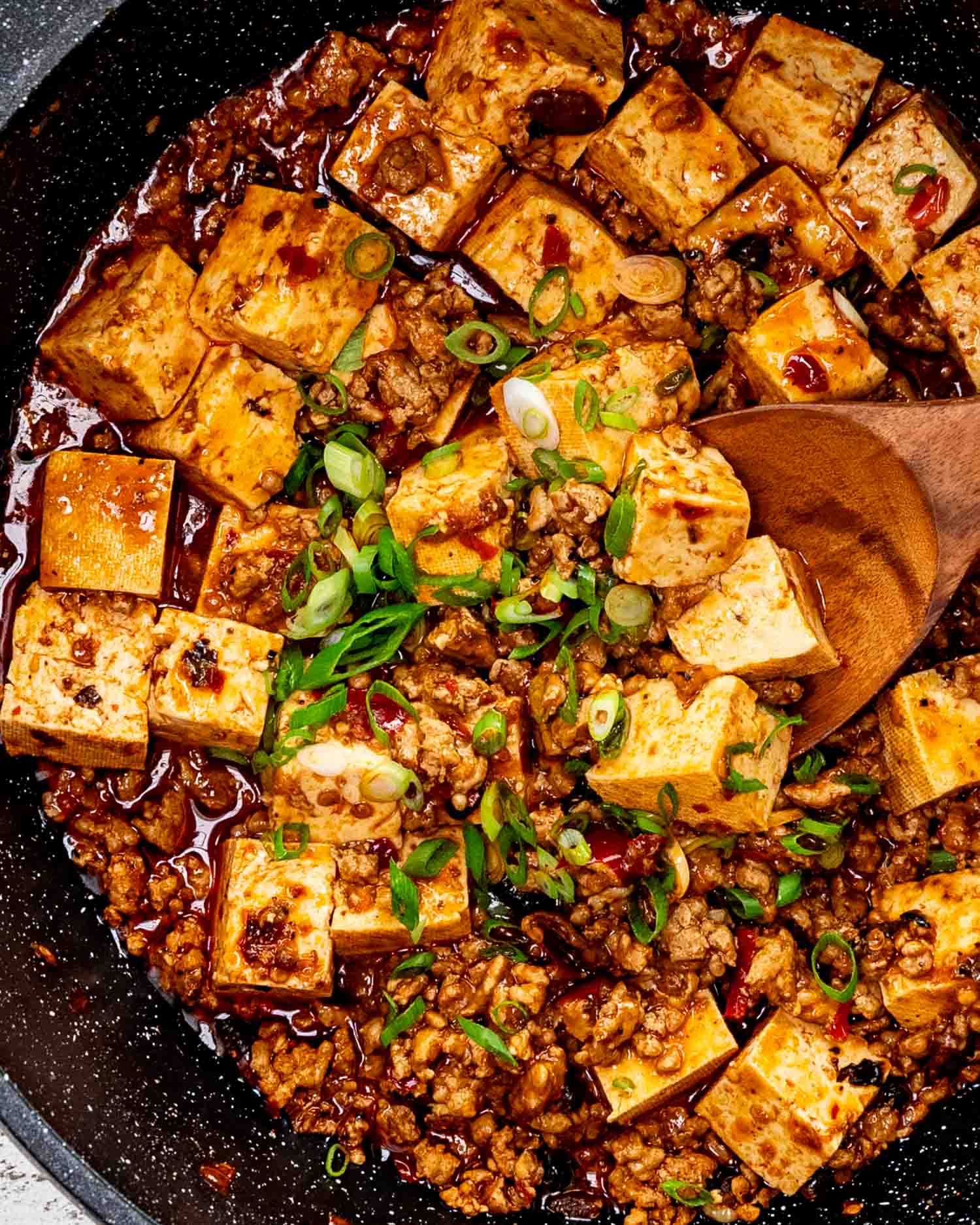 freshly made mapo tofu garnished with green onions in a skillet.