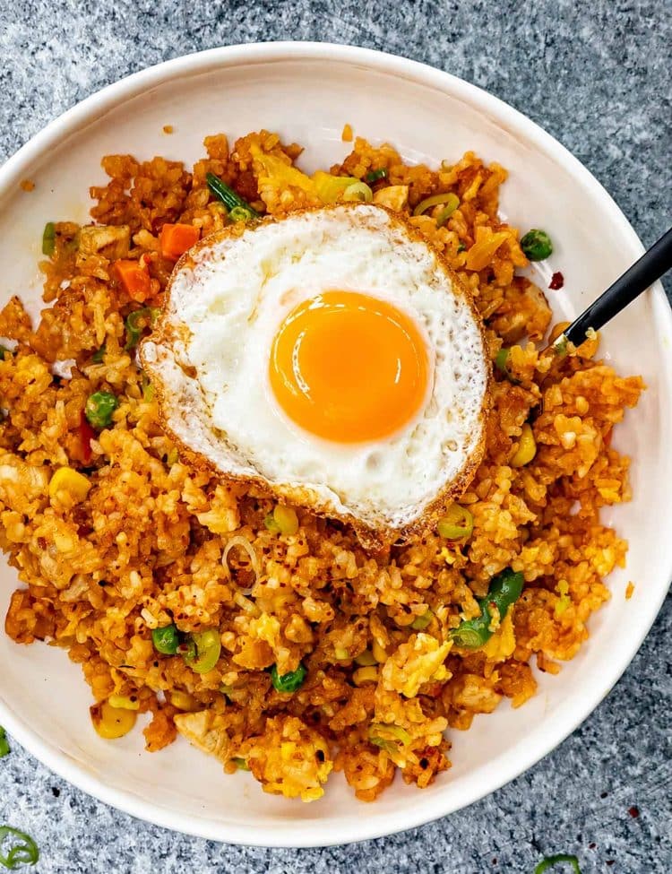 Overhead view of chicken nasi goreng with vegetables, green onions, and a crispy fried egg with golden yolk.