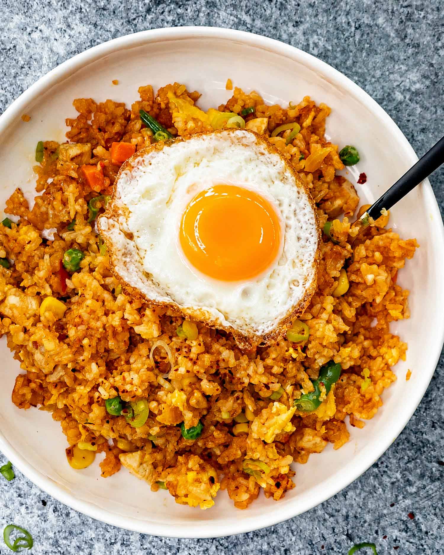 Overhead view of chicken nasi goreng with vegetables, green onions, and a crispy fried egg with golden yolk.