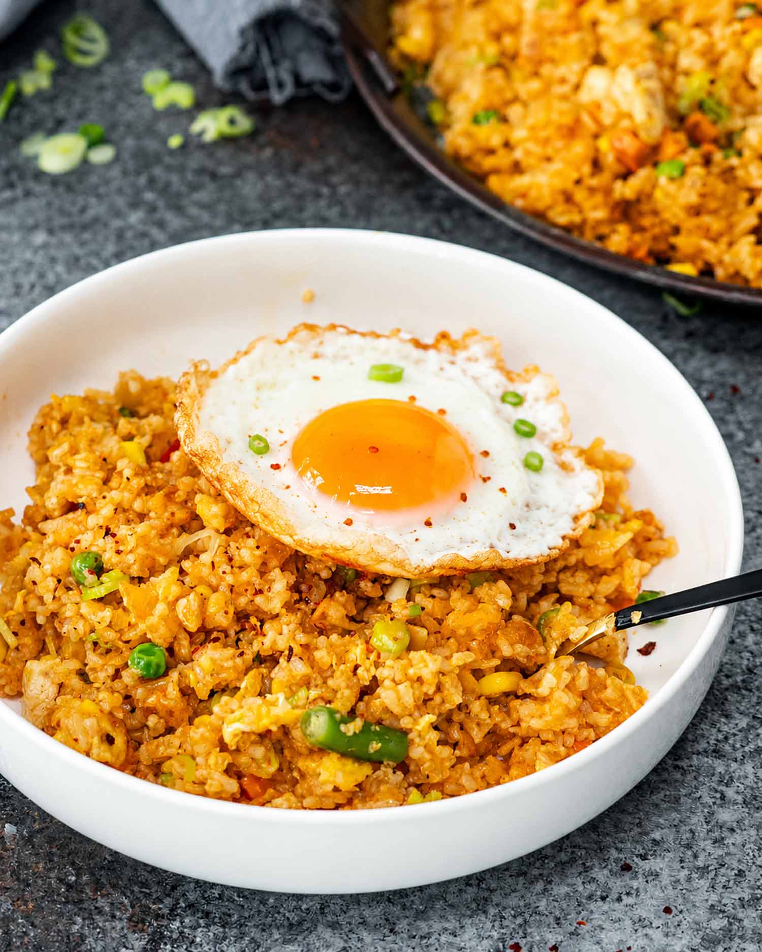 White bowl filled with colorful nasi goreng, topped with a crispy fried egg and garnished with sliced green onions.