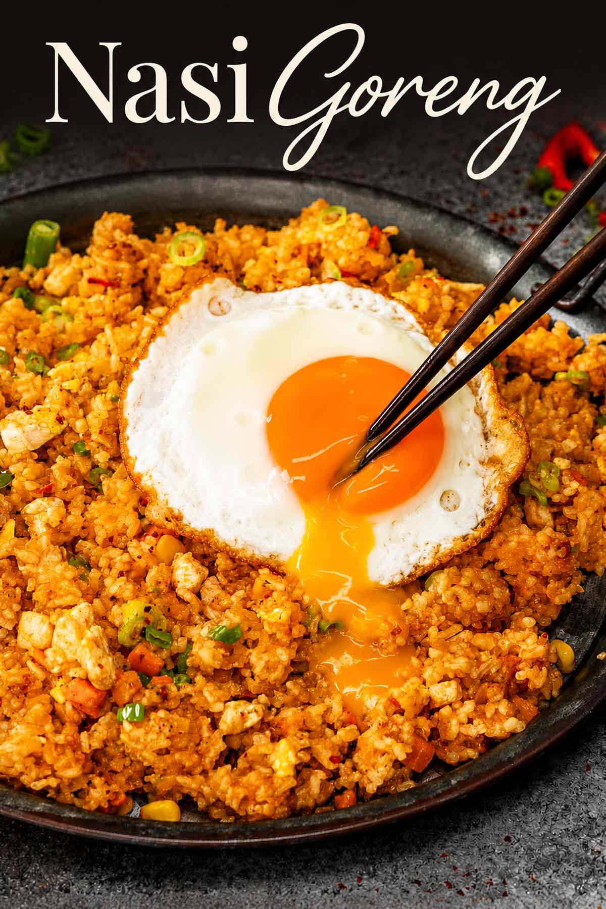 Pinterest image of nasi goreng with chopsticks breaking the fried egg yolk, sending it flowing over spicy rice.